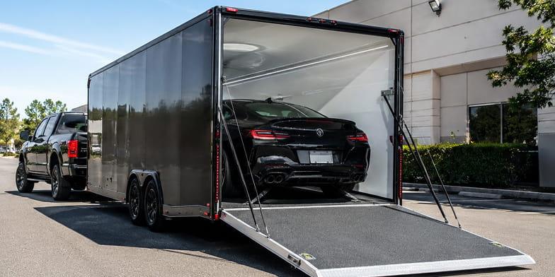 Black luxury car being loaded into an enclosed transport trailer